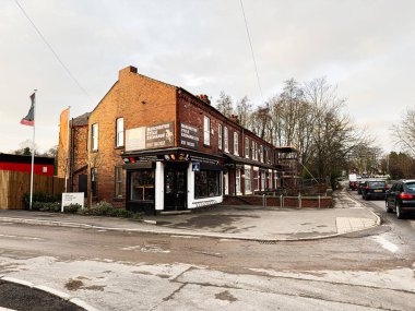 Manchester, İngiltere - 23 Ocak 2026: Manchester caddesi boyunca dükkanları, arabaları ve yayaları olan tarihi tuğla bina.