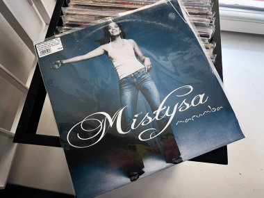 Lviv, Ukrayna - 07 Şubat 2026: Pırıl pırıl bir vinil Mistysa Macumba albüm kapağı kot pantolon giymiş bir kadın ve mavi arka planda poz veren beyaz bir atlet.