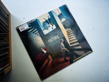 Lviv, Ukrayna - 07 Şubat 2026: Eski bir Manfred Mann 's Earth Band, Angel Station 1979 vinil kapağı rafların kenarına yaslanmış, karamsar ışıklandırma ve cesur mizah sanatını yakalıyor.