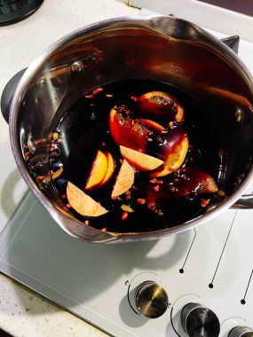 Sıcak şarap, portakal dilimleri ve baharatlarla mutfak sobasında kaynayan paslanmaz çelik bir tencerede..