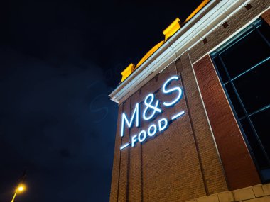 Manchester, İngiltere - 23 Ocak 2026: Manchester, İngiltere 'de bir tuğla cephede mavi bir neon M ve S Food tabelasının gece sahnesi. Marks ve Spencer.