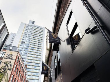 Manchester, İngiltere - 24 Ocak 2026: Tuğla duvarlara karşı Guinness sancakları ve modern binaların yer aldığı Manchester 'da sokak sahnesi.