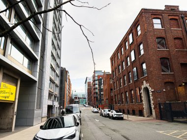 Manchester, İngiltere - 24 Ocak 2026: Vibrant Manchester Anvil Caddesi tuğla depoları, modern cam kuleleri ve kaldırım boyunca park edilmiş arabaları olan.