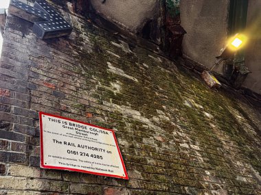 Manchester, İngiltere - 24 Ocak 2026: Manchester 'da bir sokak lambasının altındaki Büyük Marlborough Caddesi uyarı levhasının yanında Mossy tuğlası yüzeyi.