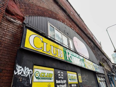 Manchester, İngiltere - 24 Ocak 2026: Manchester 'da Urban Club Radio Cars mağazası önü açık sarı bir kulüp tabelası, duvar yazısı ve kepenkli bir dükkan önü.