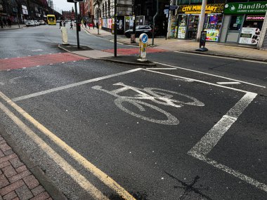 Manchester, İngiltere - 24 Ocak 2026: Kentsel bir merkezde bisiklet şeridi işaretleri, dükkan önleri ve yayalar ile Manchester sokak sahnesi.