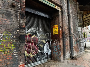 Manchester, İngiltere - 24 Ocak 2026: Manchester 'daki sokak sahnesi grafiti tuğlaları, metal kepenkler ve uyarı levhası ile.