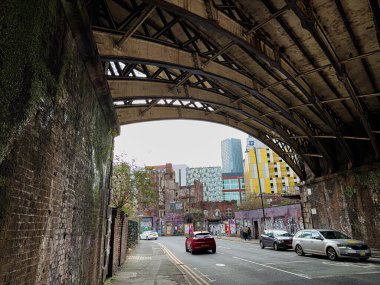 Manchester, İngiltere - 24 Ocak 2026: Manchester 'da duvarları ve park edilmiş arabaları olan çelik bir köprünün altındaki şehir sahnesi.