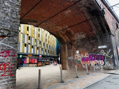 Manchester, İngiltere - 24 Ocak 2026: Tuğla kemerin altındaki şehir sahnesi graffiti, modern mağazalar ve Manchester 'daki Jack Rosenthal St Life' ı gösteriyor.