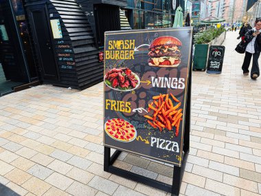Manchester, İngiltere - 24 Ocak 2026: Manchester caddesinde renkli bir açık hava menüsü reklam panosu hamburgerler, kanatlar, patates kızartmaları ve pizza.