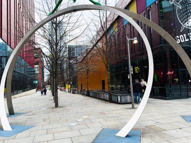 Manchester, İngiltere - 24 Ocak 2026: Manchester 'da çağdaş bir kentsel geçitte geniş bir metal dairesel çerçeve içeren bir kamu sanatı kurulumu.