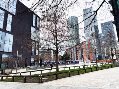 Manchester, İngiltere - 24 Ocak 2026: Manchester 'da cam kuleleri, çıplak ağaçları ve yaya geçidi olan şehir parkı sahnesi.