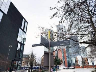 Manchester, İngiltere - 24 Ocak 2026: Manchester 'da bir şehir merkezinde sokak tabelaları ve modern binalar gösteren hareketli şehir manzarası.