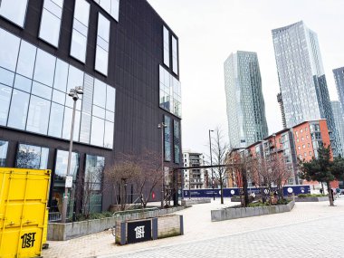 Manchester, İngiltere - 24 Ocak 2026: Manchester, İngiltere 'de cam cepheler, yaya plazası ve parlak sarı konteynır içeren ilk sokak ofisi.