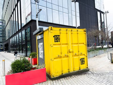 Manchester, İngiltere - 24 Ocak 2026: Manchester 'da cam bir ofis binasının yanında koyu sarı bir konteynır bulunuyor..