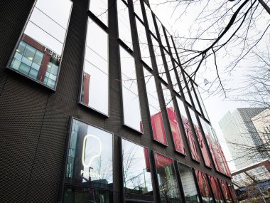 Manchester, İngiltere - 24 Ocak 2026: Manchester şehir manzarası ve çıplak dalları yansıtan uzun pencereli safkan spor salonu cam cephesi.
