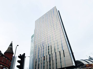 Manchester, İngiltere - 24 Ocak 2026: Modern cam eksen kulesi Manchester caddeleri üzerinde yükseliyor, istasyon yakınlarındaki kırmızı tuğladan bir taretle çelişiyor.