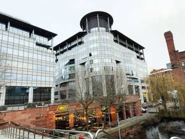Manchester, İngiltere - 24 Ocak 2026: 100 Barbirolli Meydanı mimarisi Manchester 'da bir kanal boyunca, kafe ve cam kuleler kentsel atmosfer oluşturur.