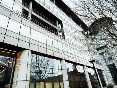Manchester, İngiltere - 24 Ocak 2026: Manchester 'da yansımaları ve çıplak ağaçları olan modern bir ofis binasının 100 Barbirolli Meydanı cephesi.