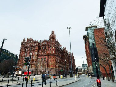 Manchester, İngiltere - 24 Ocak 2026: Manchester 'da trafiğe, yayalara ve günümüzün modern mağazalarına tepeden bakan ikonik kırmızı tuğlalı Midland Hotel mimarisi.