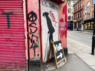 Manchester, İngiltere - 26 Ocak 2026: Manchester 'da kırmızı panjurlu şehir manzarası, Banksy duvar yazıları ve sokak köşesinde vinil karatahta tabelası.