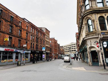 Manchester, İngiltere - 26 Ocak 2026: Kalabalık bir şehir koridoru boyunca kırmızı tuğlalı binalar, mağazalar ve yayalar bulunan canlı bir Manchester caddesi.