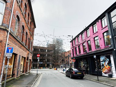 Manchester, İngiltere - 26 Ocak 2026: Manchester 'da canlı kentsel cadde pembe bir mağaza, tuğla mimari, park edilmiş bir araba ve dekoratif ışıklar sergileniyor.