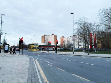 Salford, İngiltere - 28 Ocak 2026: Sarı otobüs, yayalar, trafik ışıkları ve uzun apartman blokları ile dolu Salford caddesi.
