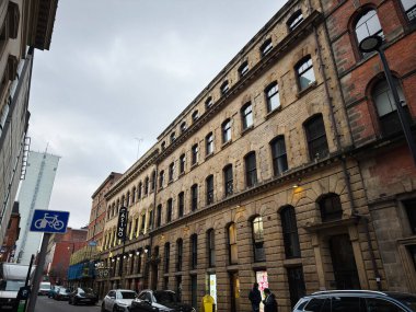 Manchester, İngiltere - 29 Ocak 2026: Manchester 'da şehir sokak sahnesi tuğlalı Grosvenor Kumarhaneleri binaları, park edilmiş arabalar ve bulutlu gökyüzü altında yayalar.