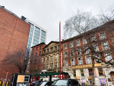 Manchester, İngiltere - 29 Ocak 2026: Manchester 'da tarihi tuğla cepheleri, modern cam binalar ve araçlarla şehir caddesi.
