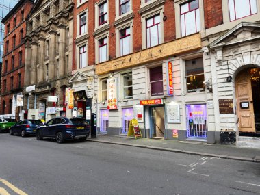 Manchester, İngiltere - 29 Ocak 2026: Tuğla binalar, Asya vitrinleri ve park halindeki arabaların yer aldığı Manchester caddesi.
