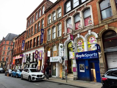 Manchester, İngiltere - 29 Ocak 2026: Tuğla binalar, çeşitli dükkanlar ve yayalar ile Manchester sokak sahnesi.