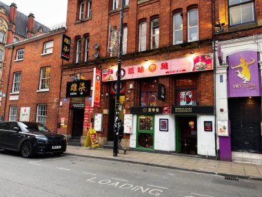 Manchester, İngiltere - 29 Ocak 2026: Manchester 'da canlı kentsel sokak sahnesi tuğla binalar ve renkli Asyalı restoran tabelaları.