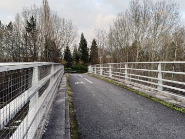 Manchester 'da bir köprüde, yapraksız ağaçlar ve bulutlu gökyüzü olan bir bisiklet yolu..