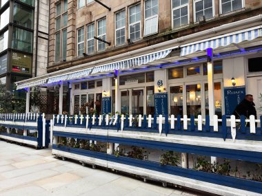 Manchester, İngiltere - 29 Ocak 2026: Manchester 'daki Street Rozafa Greek Taverna Cafe açık hava oturma, mavi tabelalı ve giriş kapısından geçen bir yolcu.