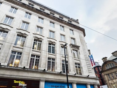 Manchester, İngiltere - 29 Ocak 2026: Manchester 'da büyük camları, sokak tabelaları ve perakende mağazaları olan zarif bir taş bina.