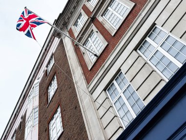Bir İngiliz bayrağı Londra 'daki tuğla ve taş bir binanın üzerinde dalgalanıyor, mimari ve şehir mirası sergileniyor..