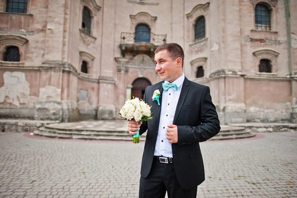 Bruidegom met boeket achtergrond oude kerk — Stockfoto