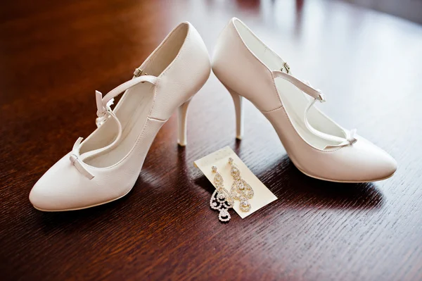 Scarpe da sposa bianche con orecchini sul tavolo di legno — Foto Stock