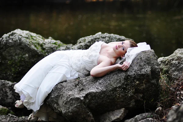 Novia acostada en las rocas del río — Foto de Stock
