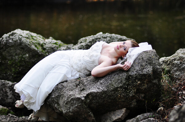 Bride lying on river rocks