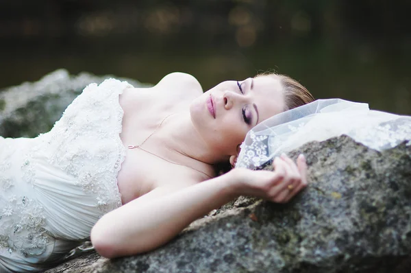 Bride lying on river rocks — Stock Photo, Image