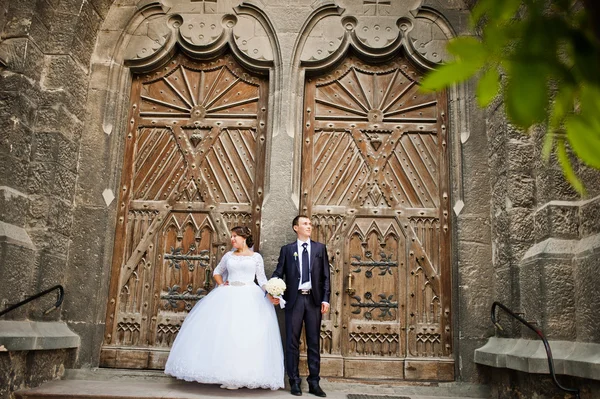 Wedding couple near old wooden door of catholic church — Stock Photo, Image