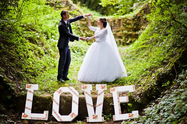 Wedding couple at green alley with big word love — Stock Photo, Image