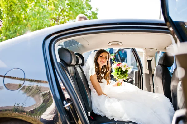 Jolie petite mariée assise à la voiture et regardant la caméra au soleil — Photo