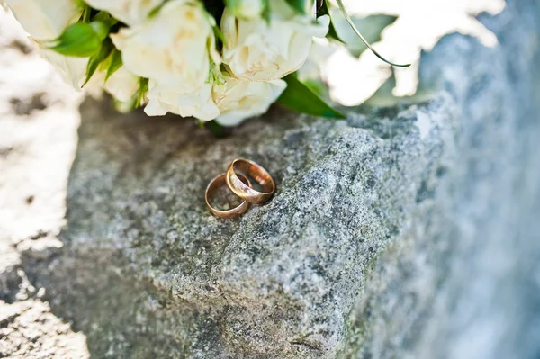 Wedding rings on stone background bouquet — Stock Photo, Image