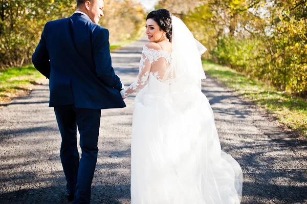 Casamento casal no fundo da estrada dia ensolarado com folhas amarelas — Fotografia de Stock