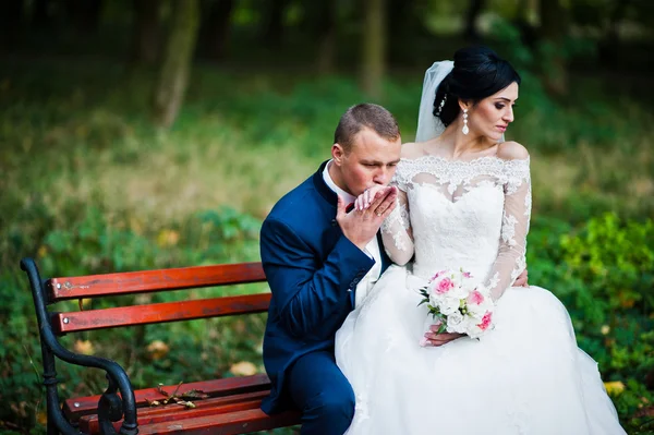 Mladé stylové Svatební pár sedící na lavičce v parku — Stock fotografie