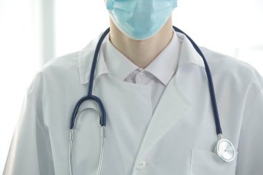 Klinikte steteskobu olan koruyucu tıbbi maskeli bir doktor.