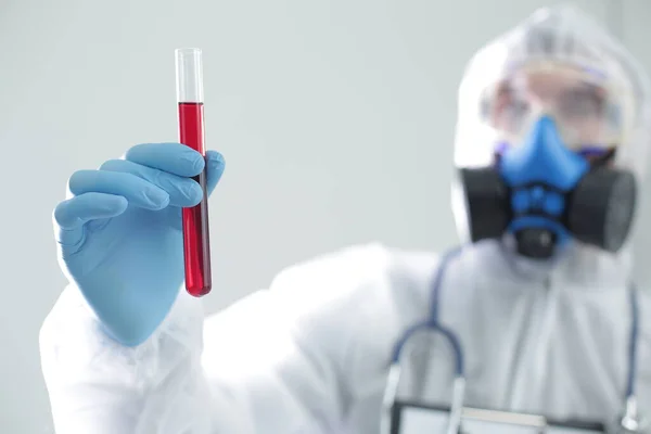 A man in protective medical suit holds a test tube in his hands. The concept of open vaccines against coronavirus